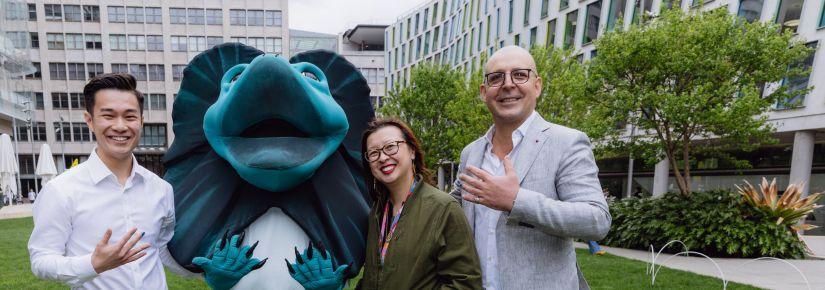 Three people and UTS mascot Lenny are standing outside, holding up their hand