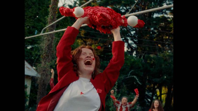 A young woman with an emotional yell holds up a pinata shaped like a uterus.