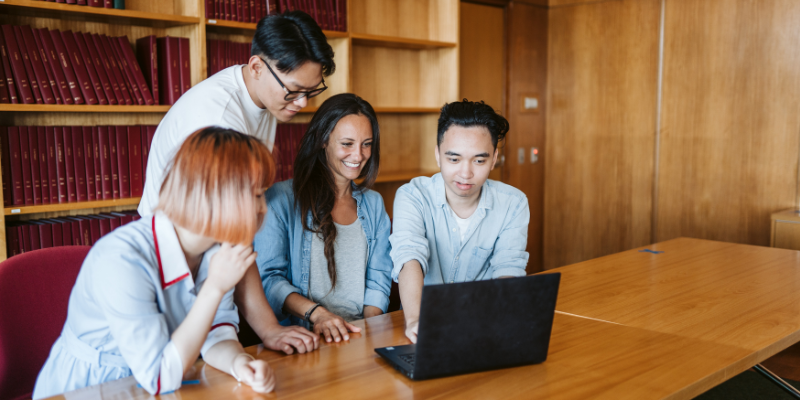 Four students sitting and looking at a laptop screen together