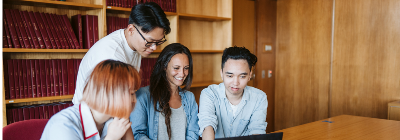 Four students sitting and looking at a laptop screen together