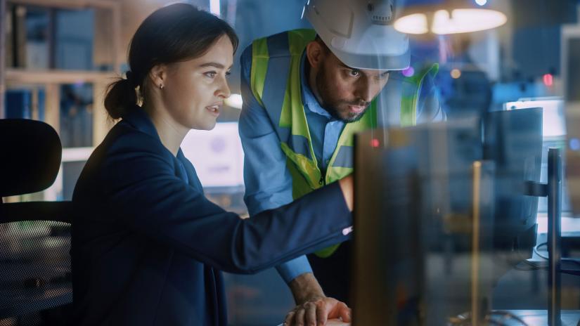 Stock picture of female industrial engineer sitting at a computer in discussion with a male project manager