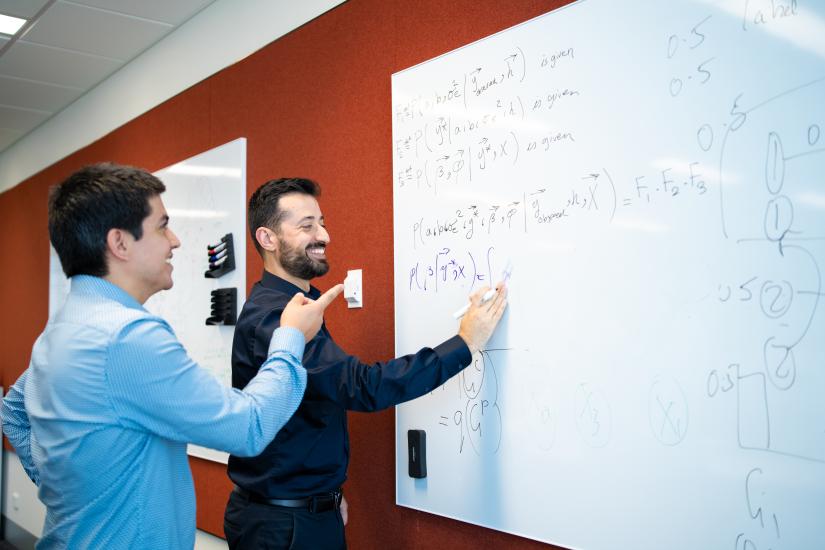 Two mean looking at and drawing formulas on whiteboard