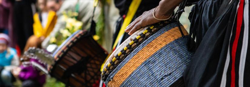 Closeup midsection of two artist performing traditional colorful string wrapped african djembe drums while standing in city during event By Valmedia