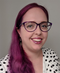 Profile picture of Sarah Kaiser smiling with dark fuchsia-coloured hair, wearing glasses and a spotty top