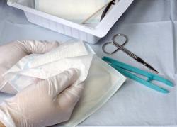 Hands in medical gloves preparing dressing tray including gauze and scissors