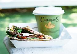 A campus coffee cup sitting in a tray with a sandwich 