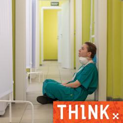 Person in scrubs sitting on hospital floor looking tired