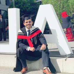 Graduate wearing mortarboard and robe sits in front of sculpture in front of two large letters L and A.
