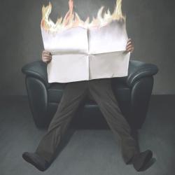 A man slumped on a couch reading a burning newspaper