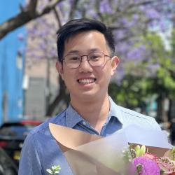Man wearing glasses and collared shirt stands holding a bouquet.