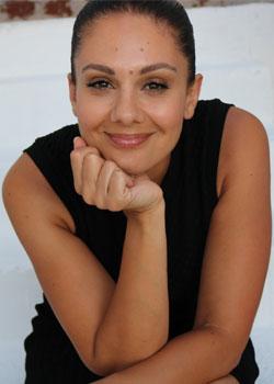 Malinda Zerefos smiling and looking at the camera with her chin resting in her hands, wearing a black sleeveless dress