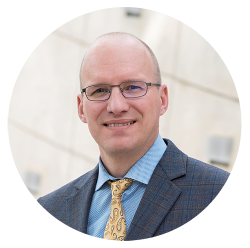 Professor William Dale wears glasses. He is wearing a suit with a blue shirt and a yellow paisley tie.