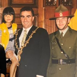 Man in mayoral robes holding young girl, beside man in army uniform