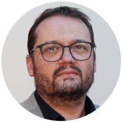 Man wearing black round glasses with a beard looking at the camera