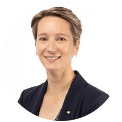 Woman with short light hair smiling and looking at the camera wearing a navy blue jacket