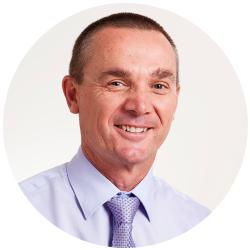 Man smiling and looking at the camera wearing a lavender shirt and a purple tie 