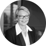 Woman with short hair and glasses in a black suit jacket and a white business shirt smiling and looking at the camera