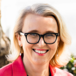 Woman with glasses, blonde hair, wearing pink jacket